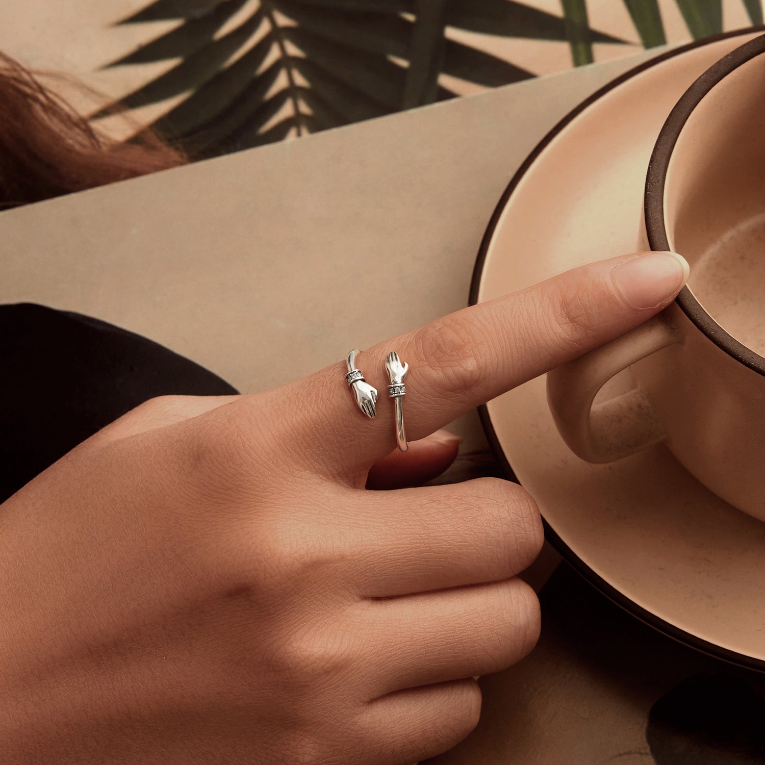 Hand with silver ring holding a ceramic cup, with a blurred natural background